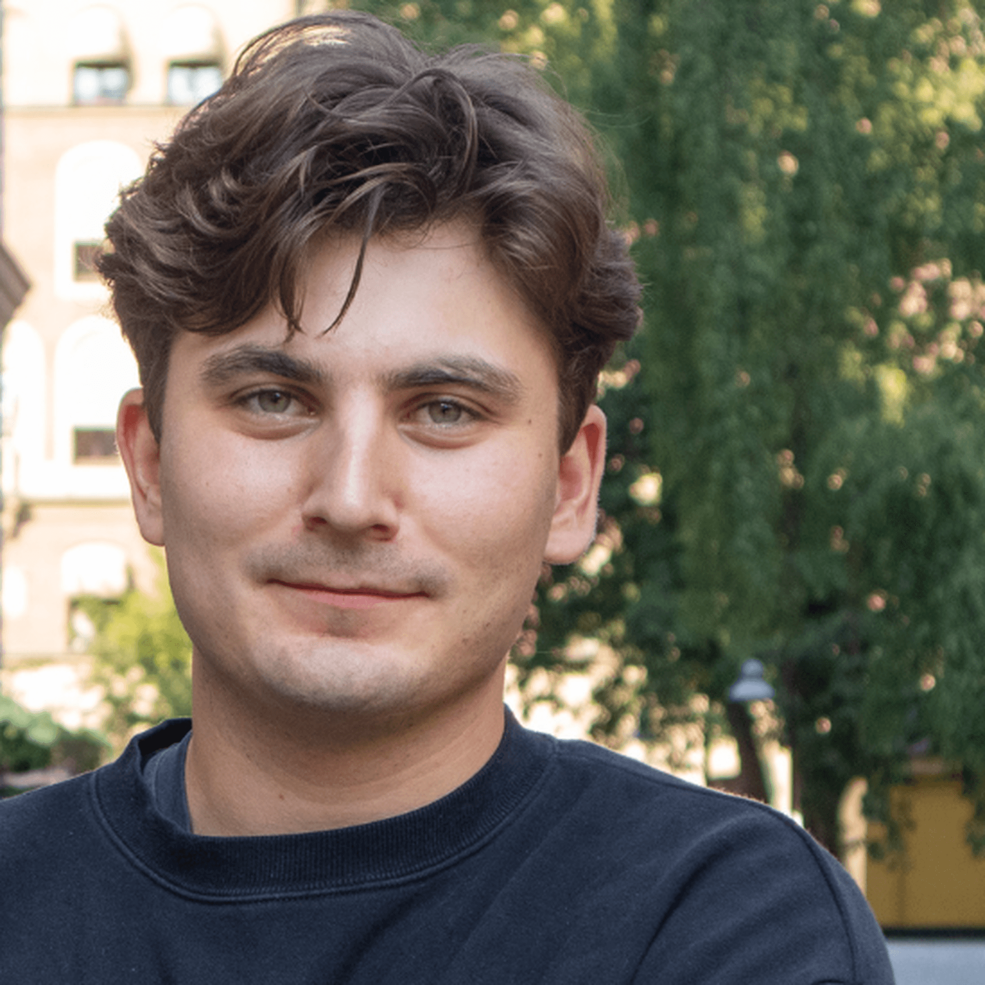 Anton utomhus med gröna träd i bakgrunden iklädd mörkblå tröja och med armarna i kors