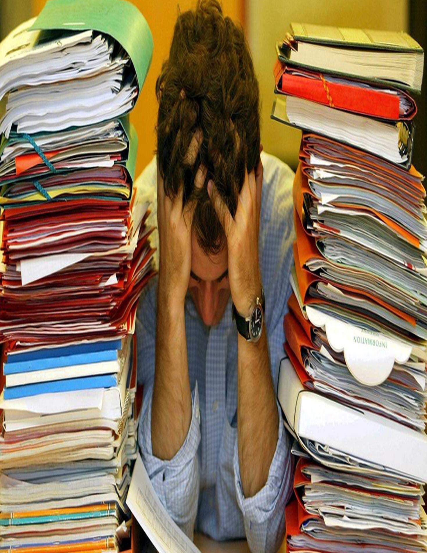 Man som bekymrat tittar ner i bordet omgiven av stora pappershögar