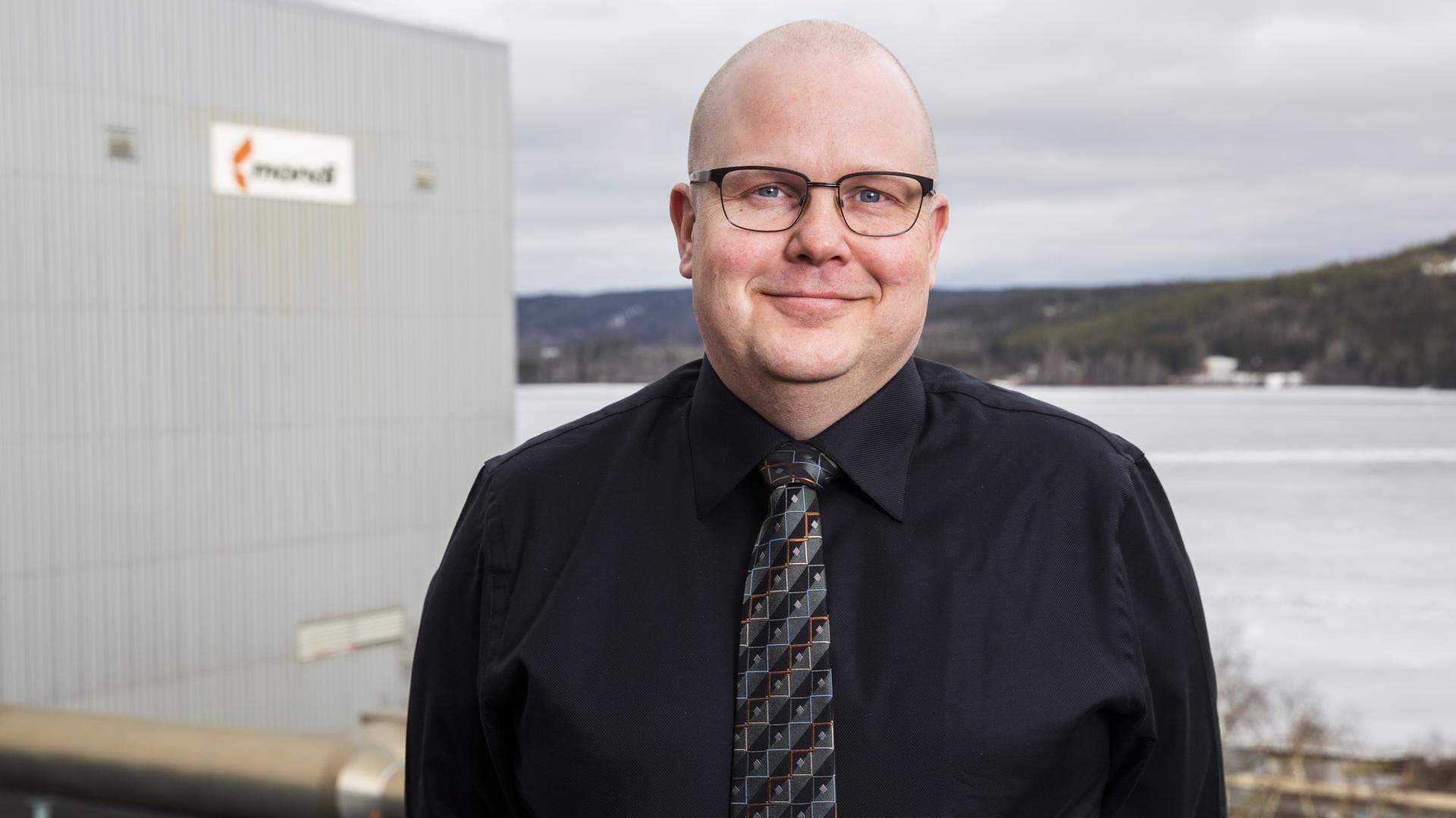 Mikael Ekholm, logistikchef på Mondi Dynäs står utomhus i industrimiljö och har en svart skjorta och slips.