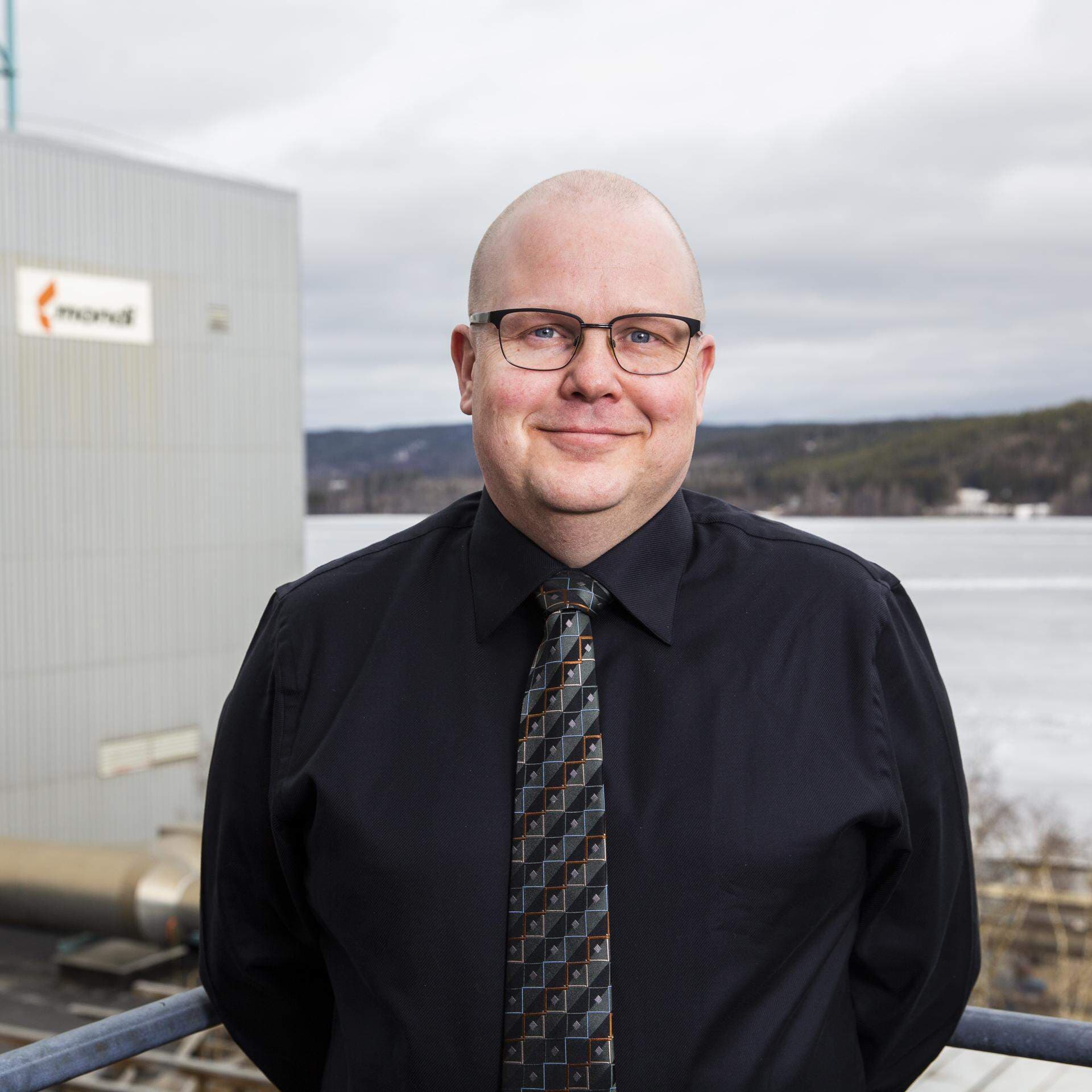 Mikael Ekholm, logistikchef på Mondi Dynäs står utomhus i industrimiljö och har en svart skjorta och slips.