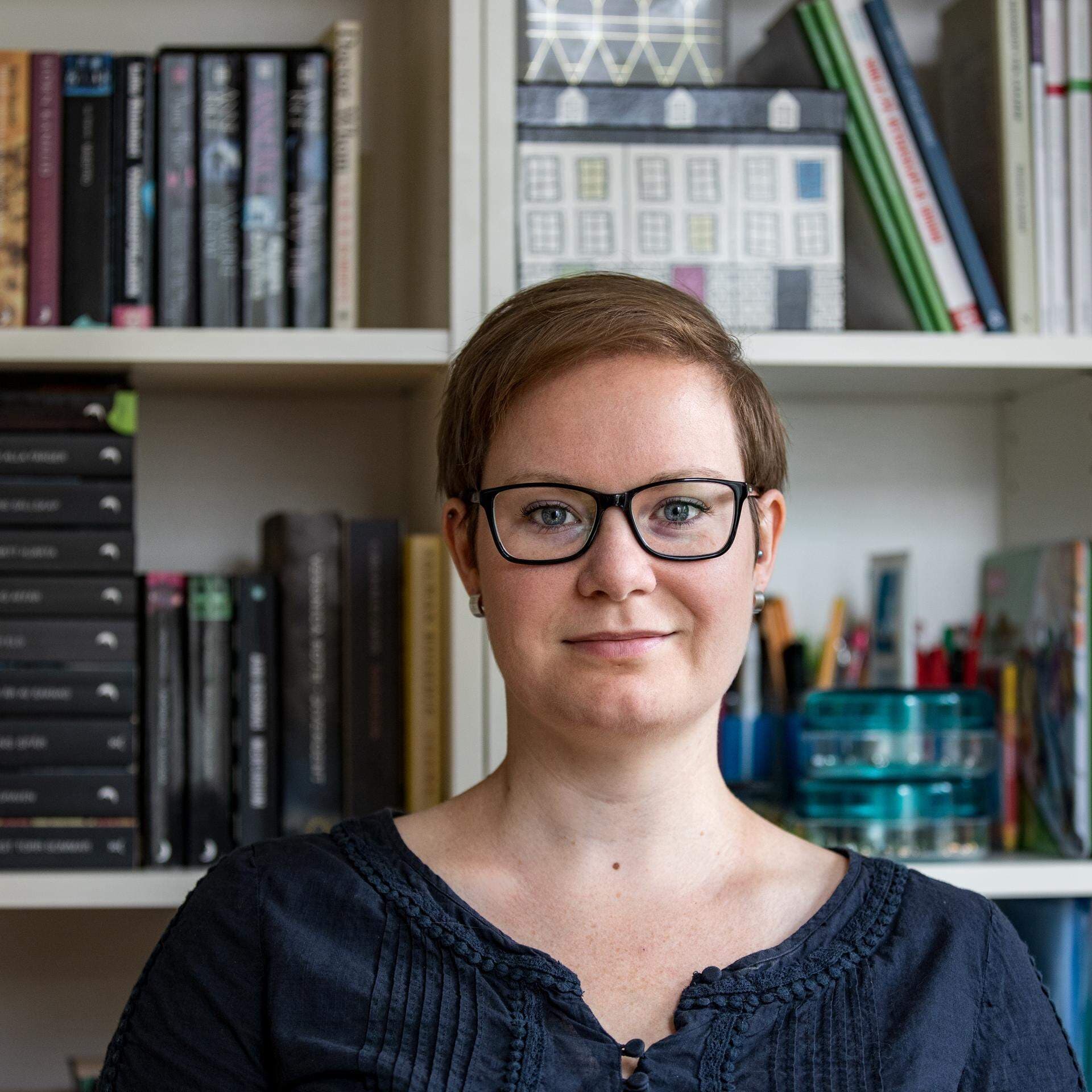 Bild på Sandra Haag framför en bokhylla fylld med stående och liggande böcker