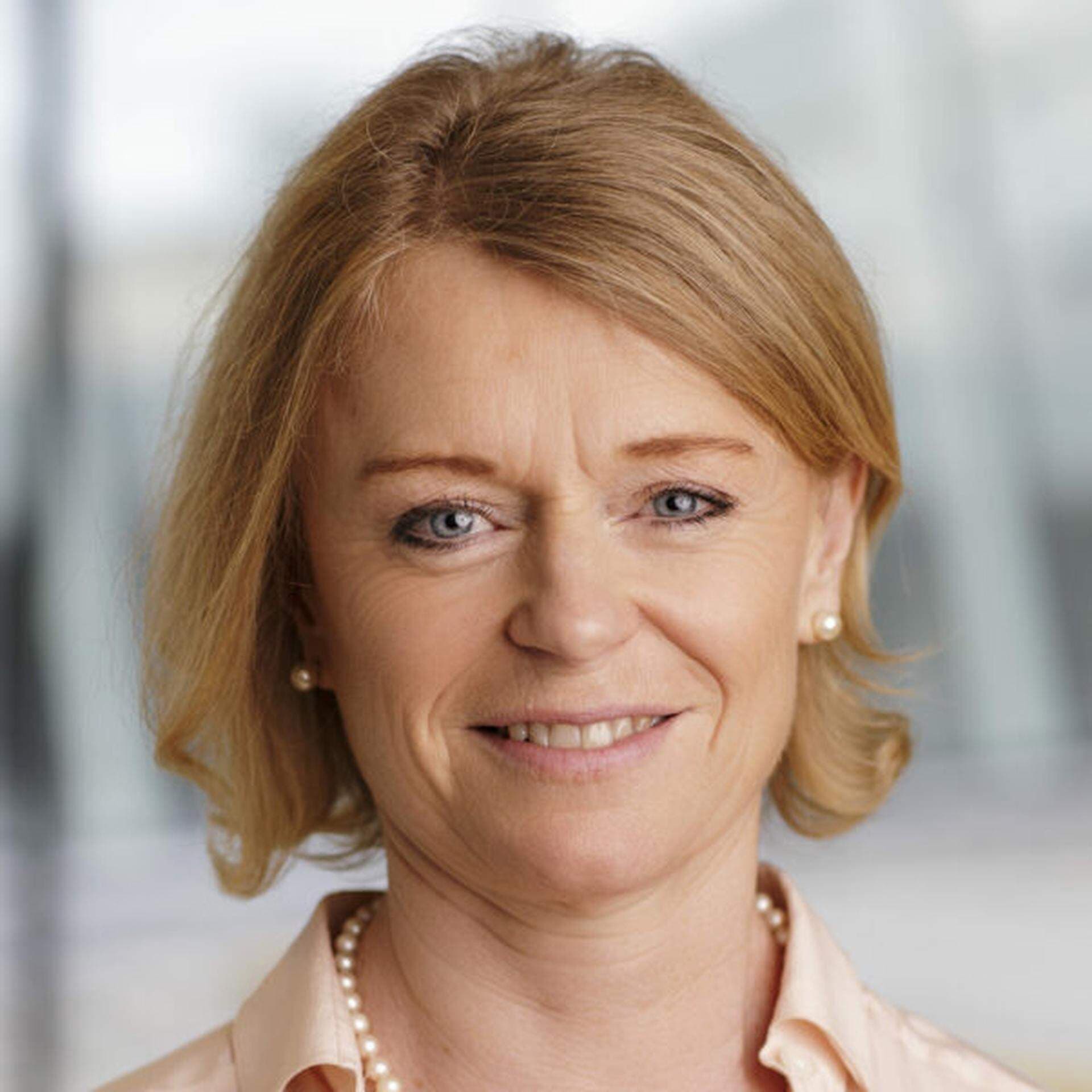 Karin Thapper i rosa/beige blus, pärlssmycken och grå bakgrund