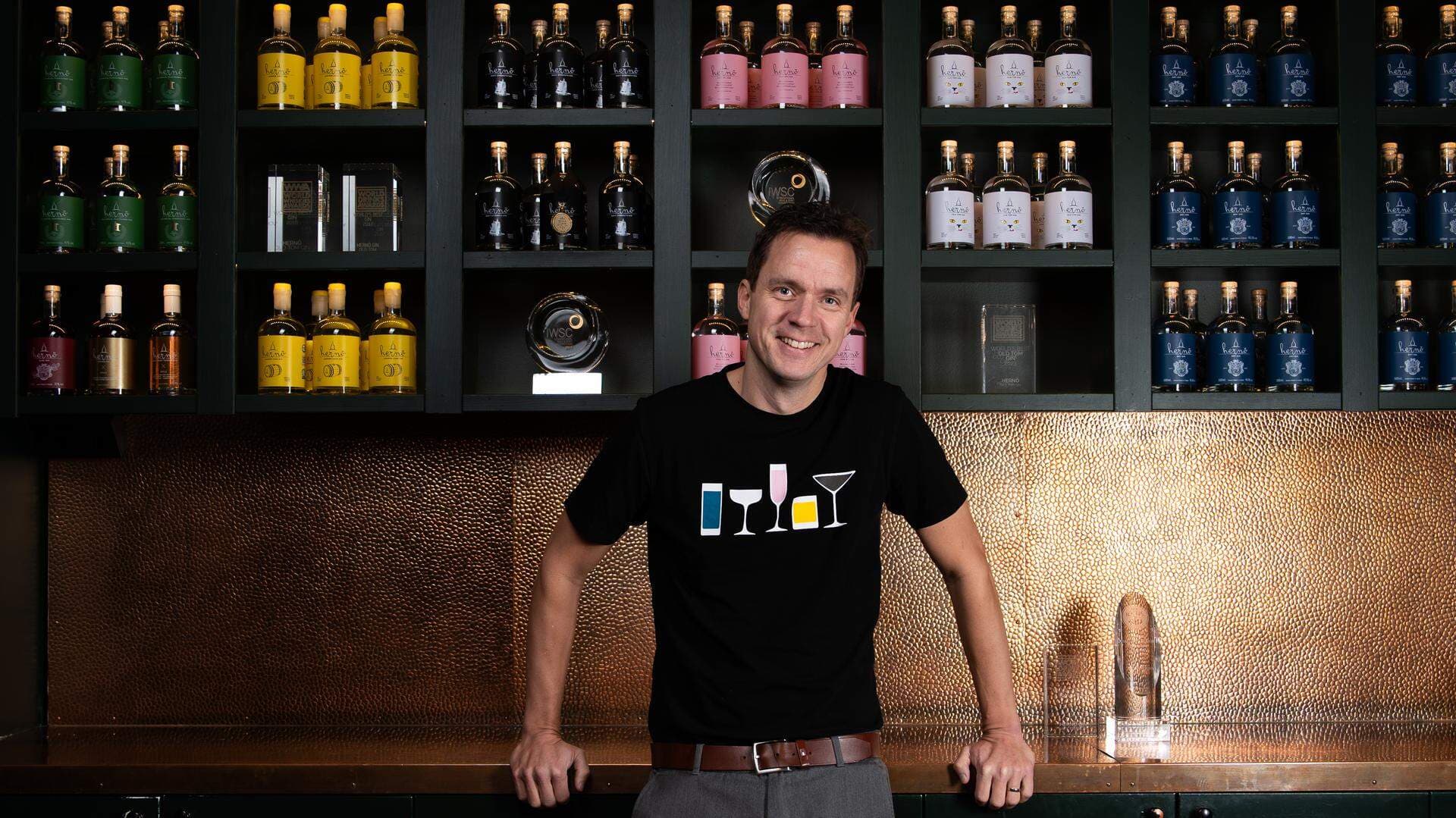 Jon Hillgren, grundare av Hernö Gin, står i destilleriet med flaskor i bakgrunden.