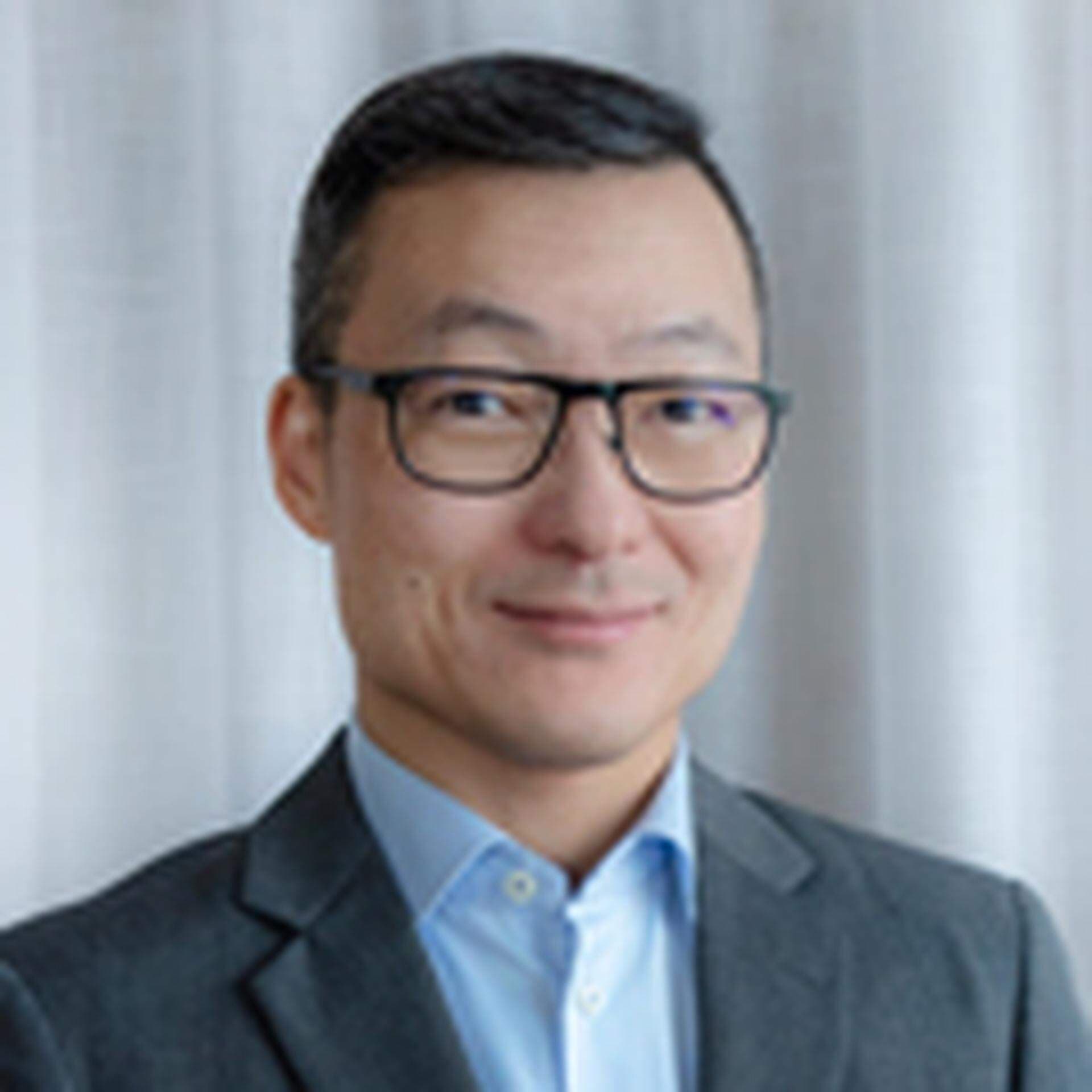 Bilden föreställer en glad man i kavaj och glasögon.