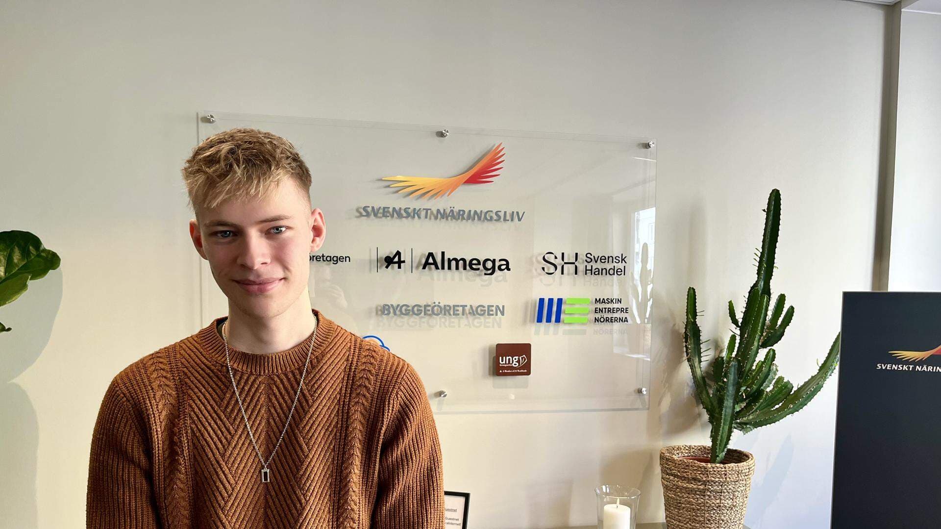 Oliver Lindgren har en orange tröja och står framför en tavla