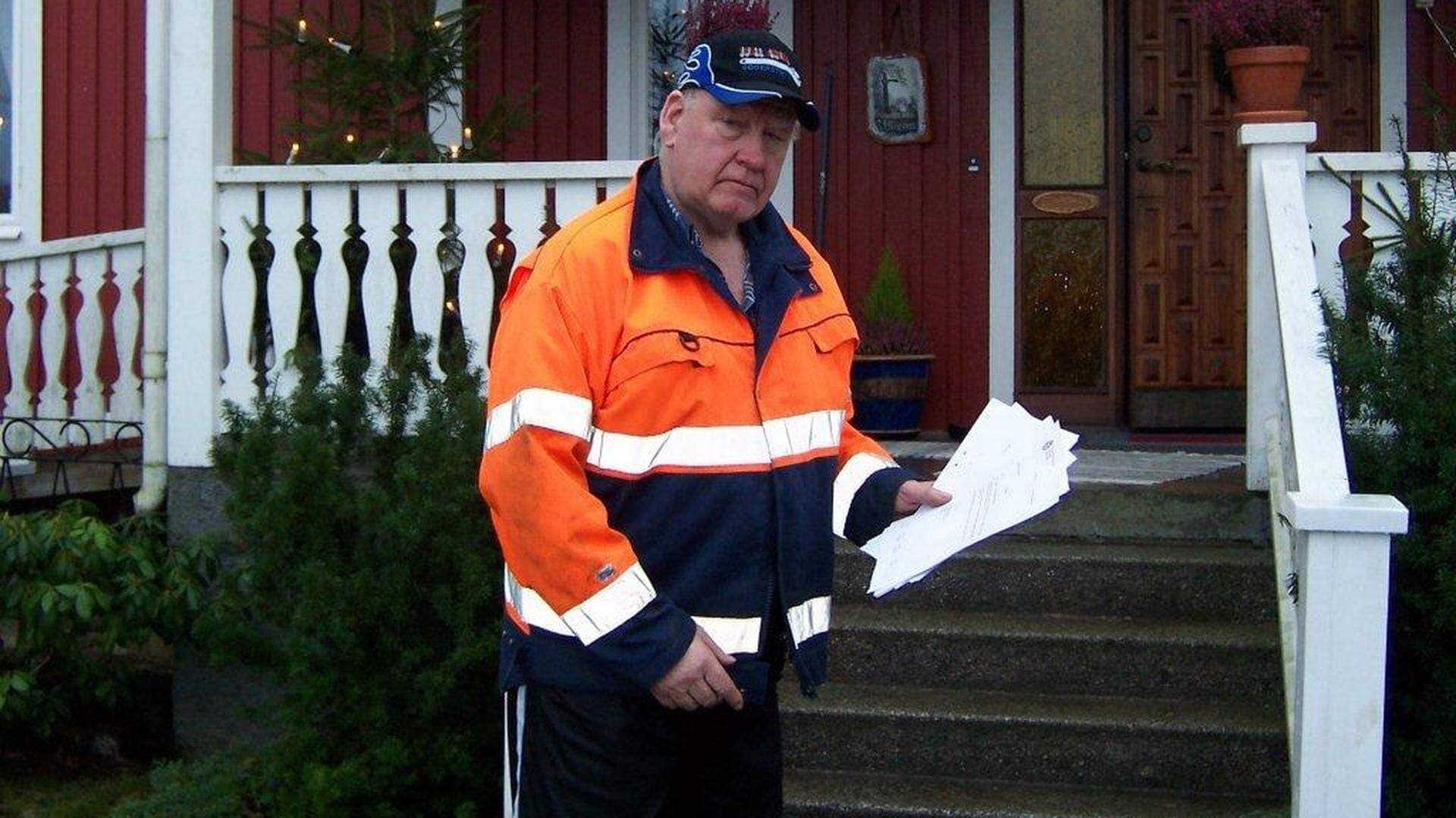 Bengt Södersten, åkeriägare, står utanför ett rött hus och håller i böteslappar.