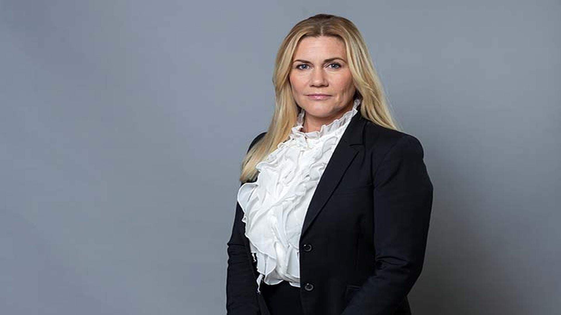 Sophia Metelius i vit blus och svart kavaj. Bakgrunden är grå