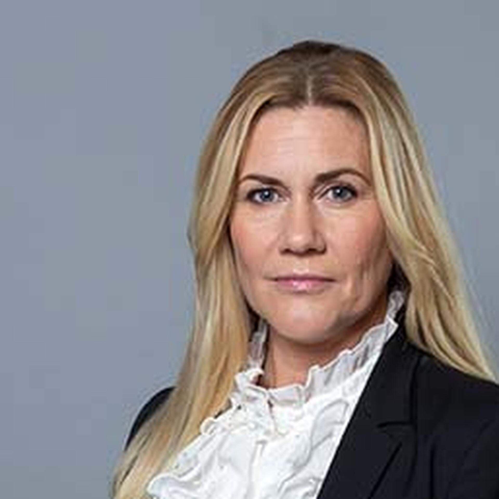 Sophia Metelius i vit blus och svart kavaj. Bakgrunden är grå