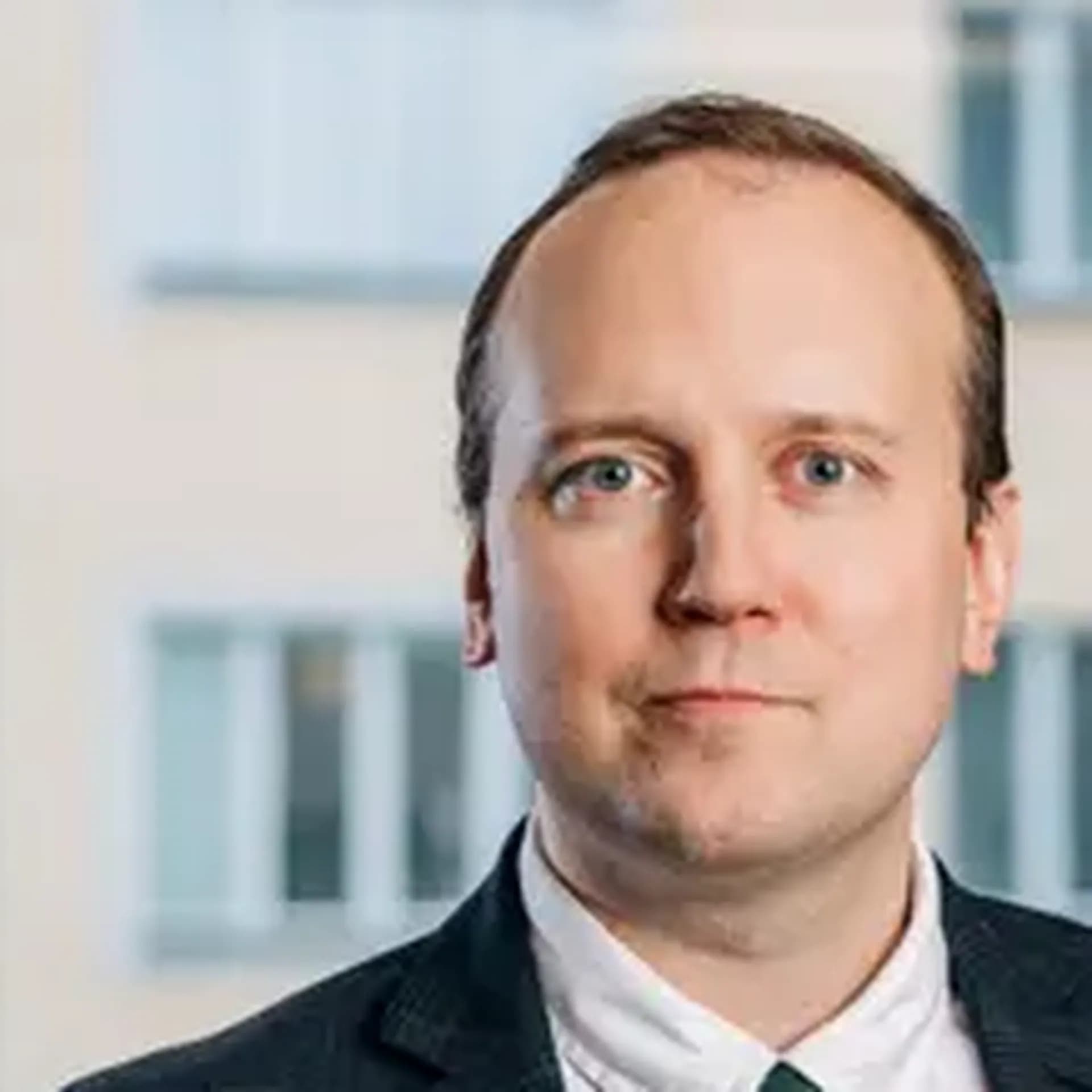 Jonas iklädd vit skjorta, mörkgrön slips och mörkblå kavaj