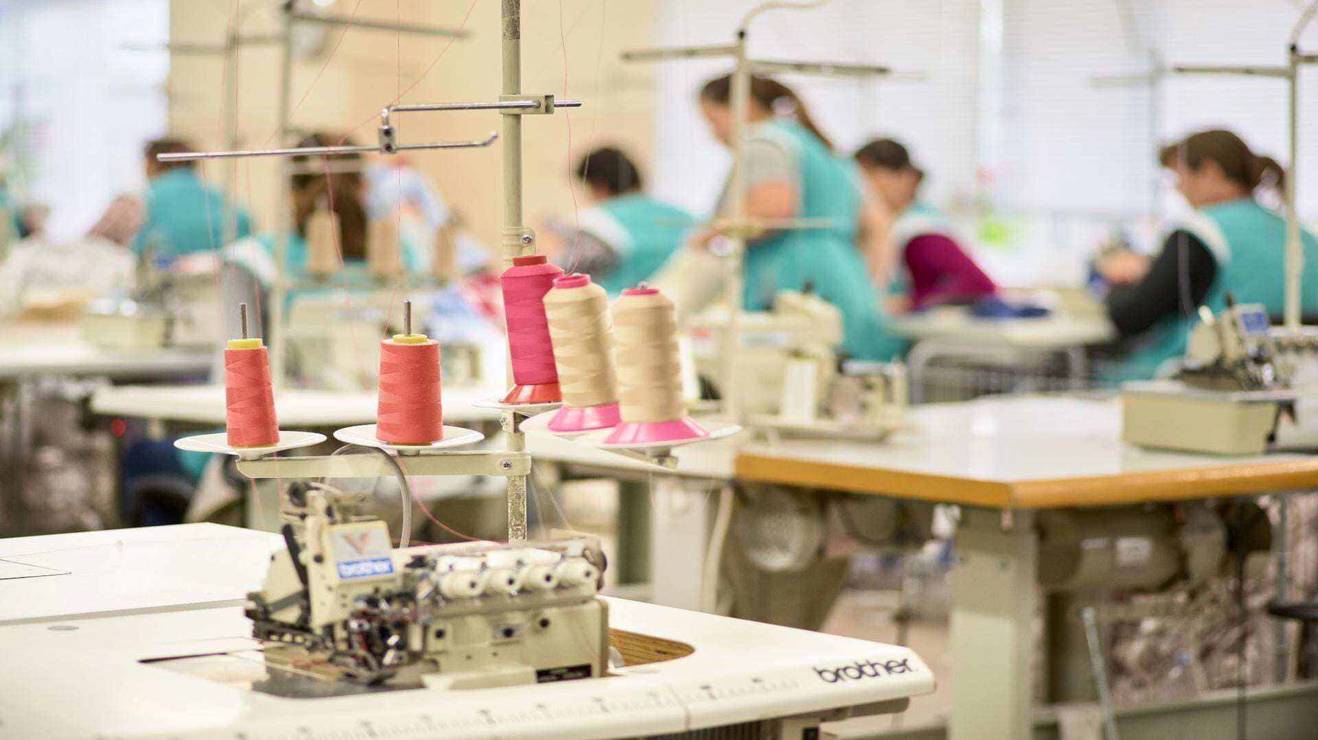 Symaskin i förgrunden och sömmerskor i bakgrunden