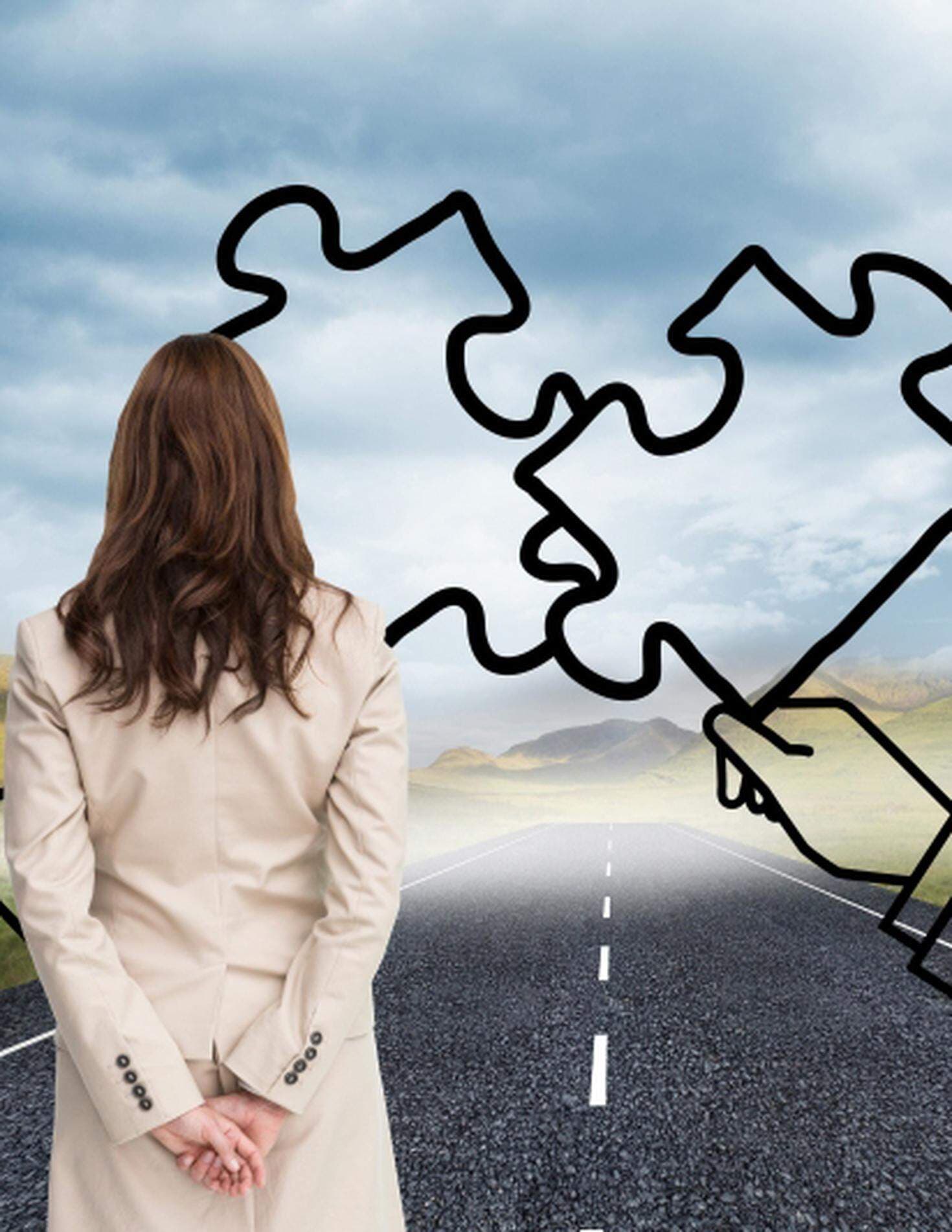 kvinna sedd bakifrån ståendes på en vägg med två ritade pusselbitar framför sig på en grå himmel